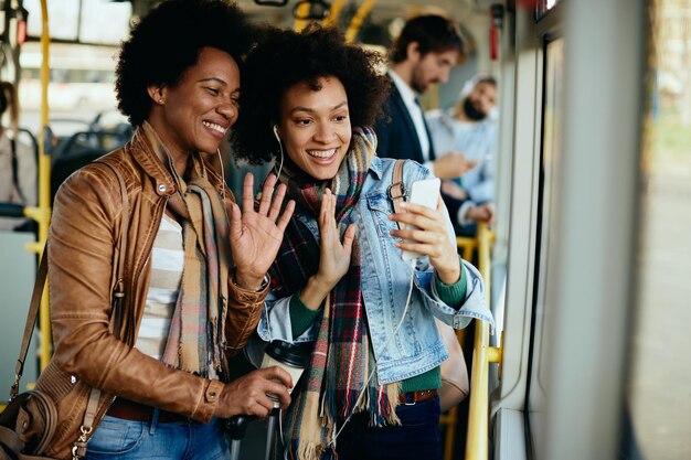 Glückliche afroamerikanische frauen, die beim pendeln in öffentlichen verkehrsmitteln einen videoanruf über ein smartphone haben