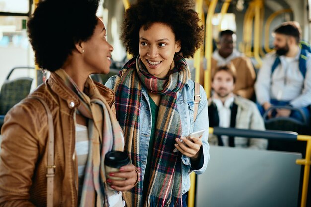 Glückliche afroamerikanische Freundinnen unterhalten sich beim Pendeln mit dem Bus