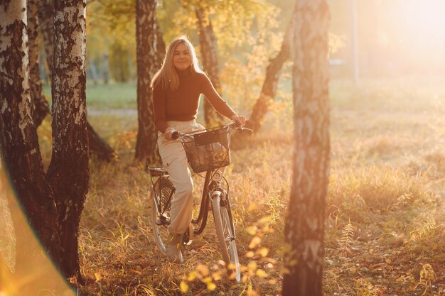 Glückliche aktive junge frau, die bei sonnenuntergang vintage-fahrrad im herbstpark reitet.