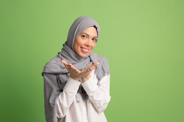 Glückliche arabische Frau im Hijab. Porträt des lächelnden Mädchens, das am grünen Studiohintergrund aufwirft.