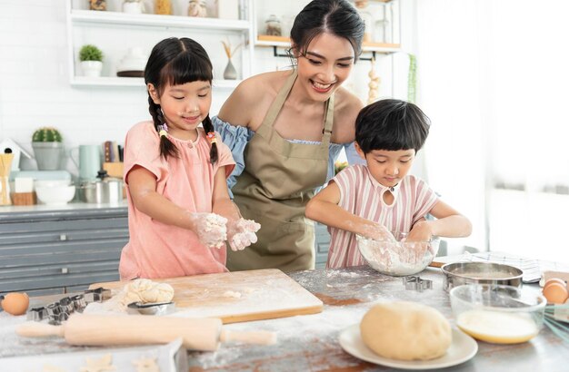 Glückliche asiatische Familie bereitet Teig zu und backt Kekse in der Küche zu Hause