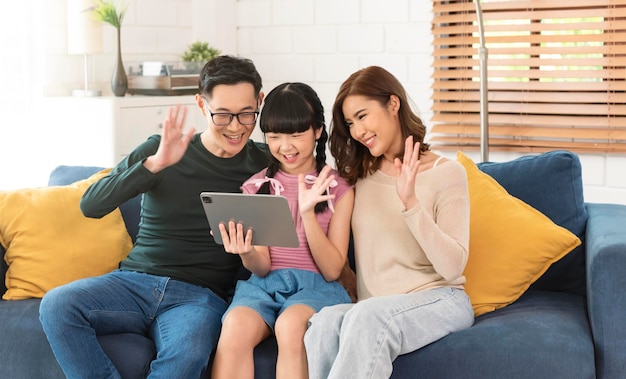 Glückliche asiatische Familie, die ein virtuelles Treffen mit Tablet-Videoanrufen auf dem Sofa zu Hause im Wohnzimmer nutzt