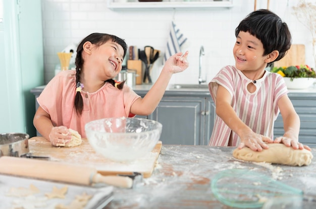 Glückliche asiatische familienlustige kinder bereiten den teig backkekse in der küche zu
