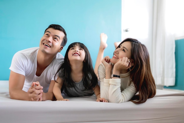 Glückliche asiatische Familienmutter, Vater und Tochter, die ein lustiges Schlafspiel im Hintergrund des Wohnzimmers machen