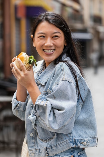 Kostenloses Foto glückliche asiatische frau, die einen burger draußen isst