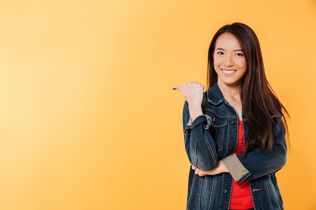 Glückliche asiatische Frau in der Denimjacke weg zeigend auf copyspace