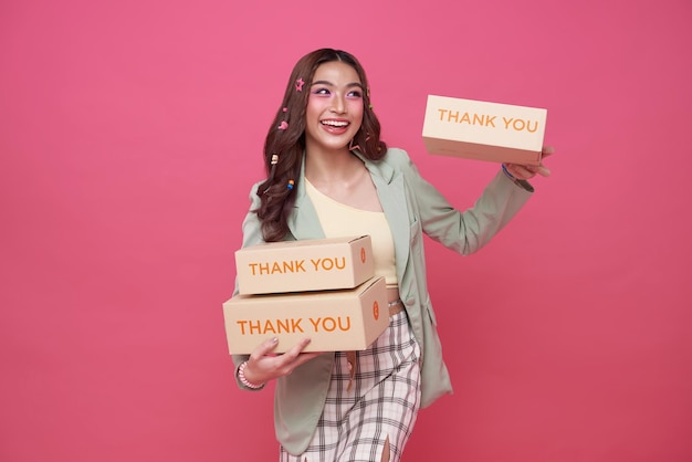 Glückliche asiatische Frau lächelt und hält Paketpaketbox isoliert auf rosa Hintergrund