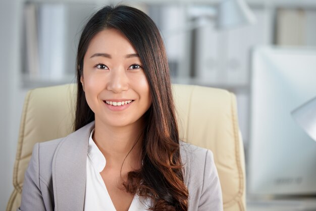 Glückliche asiatische Geschäftsdame, die im Büro und im Lächeln sitzt