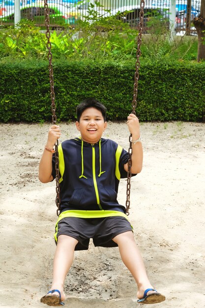 Glückliche asiatische Sport Junge spielen auf Swing Spielplatz im Garten.