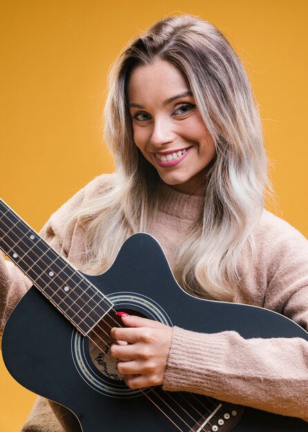 Glückliche attraktive Frau, die Gitarre gegen gelben Hintergrund spielt