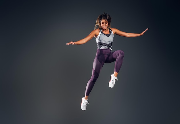 Glückliche attraktive Frau in Activewear springt im Studio über grauem Hintergrund.