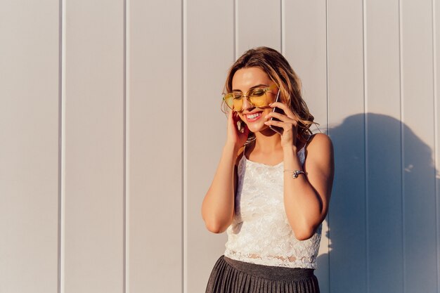 Glückliche attraktive Frau in der gelben Sonnenbrille, die Telefongespräch hat