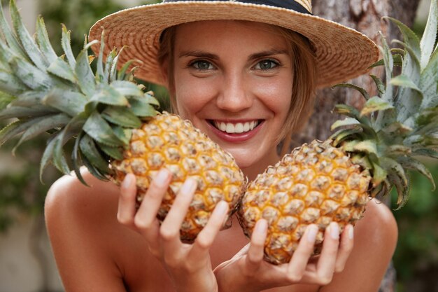 glückliche attraktive Frau mit breitem Lächeln, hält zwei Ananas