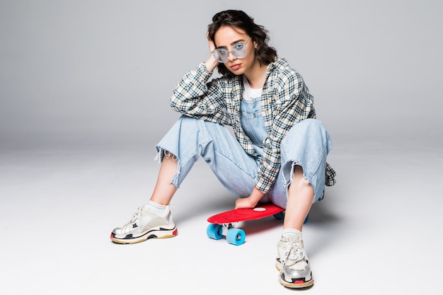 Glückliche attraktive junge Frau in der Sonnenbrille, die auf Skateboard sitzt