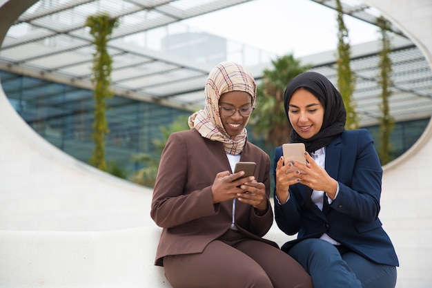 Glückliche aufgeregte kollegen, die auf smartphones plaudern