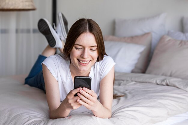 Glückliche Bloggerin auf dem Bett mit ihrem Smartphone