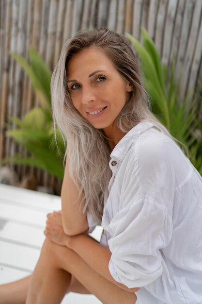 Glückliche blonde Frau in weißer Bluse posiert im tropischen Resort Reise- und Urlaubskonzept