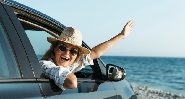 Glückliche blonde Frau mit Hut, der aus Autofenster schaut