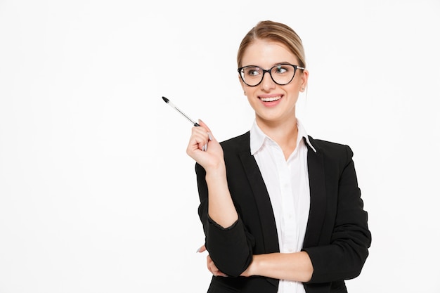 Glückliche blonde Geschäftsfrau in Brillen mit Stift in der Hand, die Idee hat und über weiße Wand wegschaut