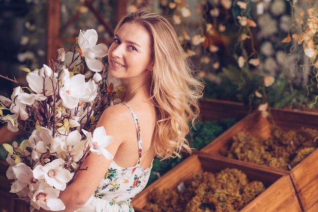 Glückliche blonde junge Frau, die in der Hand Kamelienblumenstrauß hält