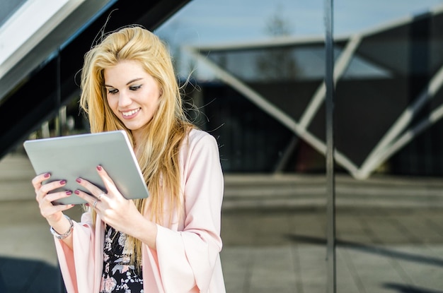 Glückliche blonde junge Frau im Freien mit ihrem Tablet