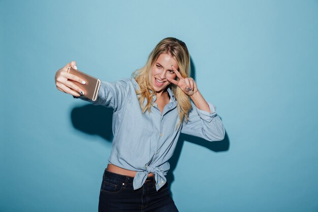 Glückliche Blondine im Hemd, das selfie auf Smartphone macht