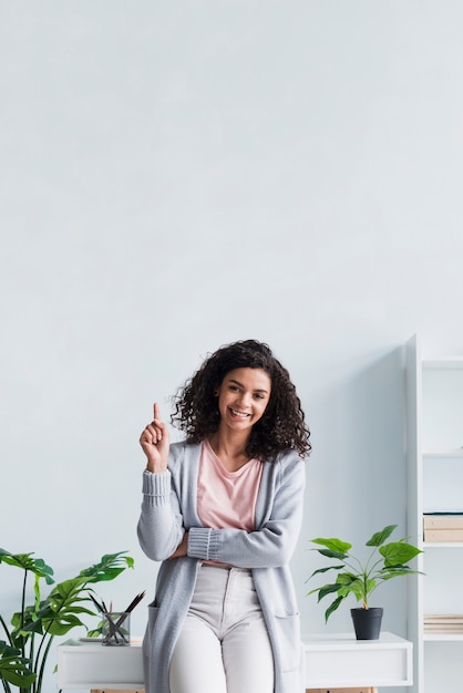 Kostenloses Foto glückliche brunettefrau, die oben an arbeitsplatz zeigt