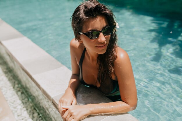 Glückliche charmante europäische Dame mit langen dunklen Haaren ruht auf Resort und schwimmt im Pool an sonnigem warmem Tag