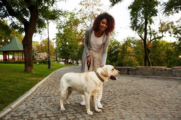 Glückliche Dame, die ihren weißen freundlichen Hund beim Gehen im Park umarmt