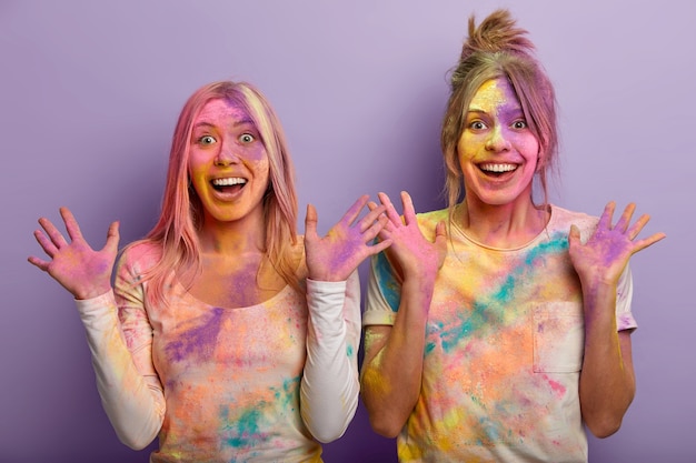 Glückliche Damen sehen ähnlich aus, haben die Haut mit buntem Puder überzogen, zeigen mehrfarbige Palmen, feiern Holi-Feiertage im März, kommen auf das dynamische Farbfestival in Indien, spritzen sich gegenseitig