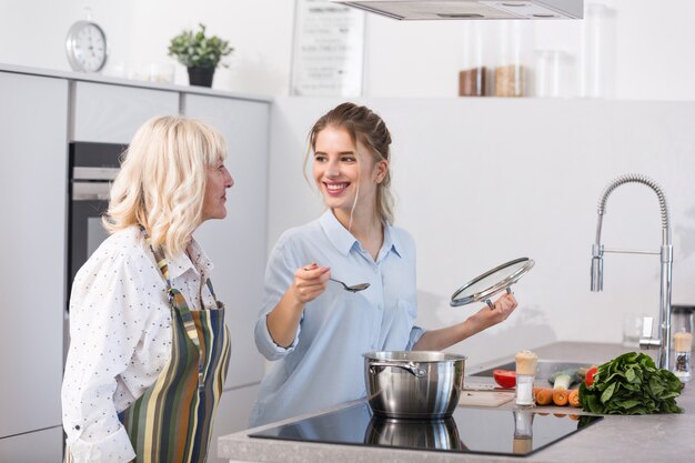 Glückliche Enkelin und ihre Großmutter kochen Gemüsesuppe