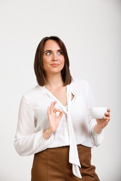 Glückliche erfolgreiche Frauenshow okay, geben Sie Zustimmung, trinken Sie Kaffee