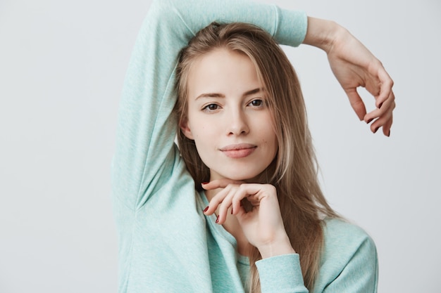 Glückliche erfreute blonde frau des europäischen aussehens mit dunklen augen, die blaues langärmeliges oberteil tragen und lächeln