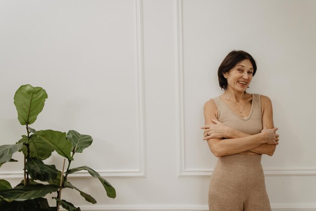 Glückliche erwachsene kaukasische brünette Frau, die vor weißem Wandhintergrund mit Platz für Text in die Kamera lächelt Freizeit-Lifestyle- und Beauty-Konzept