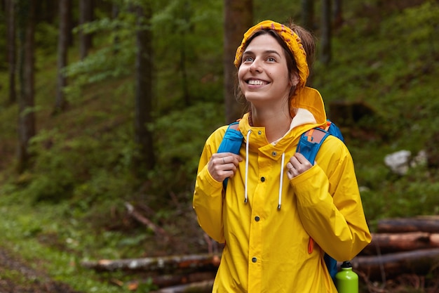 Glückliche europäische Frau mit entzücktem Ausdruck, schaut nach oben, ist gut gelaunt, atmet frische Waldluft