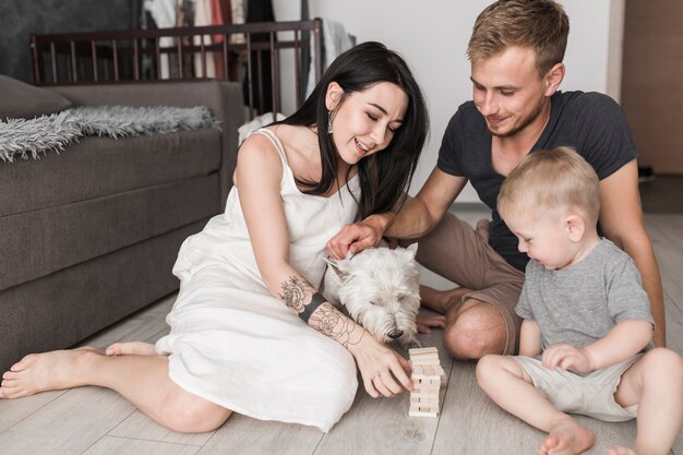 Glückliche Familie, die ein hölzernes Turmspiel der Blöcke mit Hund spielt