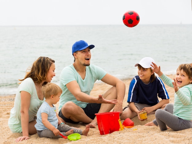 Glückliche Familie, die mit Ball am sandigen Strand spielt