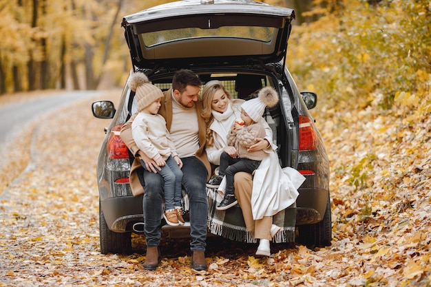 Glückliche Familie, die sich nach einem Tag im Freien im Herbstpark ausruht. Vater, Mutter und zwei Kinder sitzen im Kofferraum und lächeln. Familienurlaub und Reisekonzept.