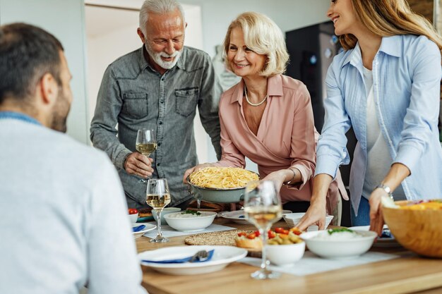 Glückliche Familie, die spricht, während sie den Esstisch für das Mittagessen vorbereitet. Der Fokus liegt auf der älteren Frau