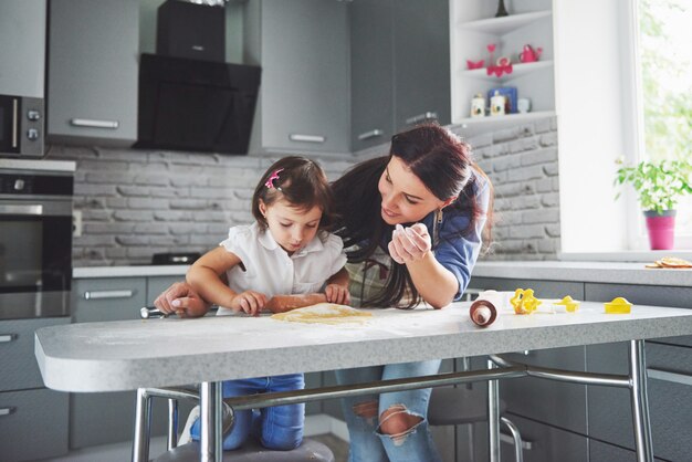 Glückliche Familie in der Küche. Holiday Food Konzept. Mutter und Tochter bereiten den Teig vor und backen Kekse. Glückliche Familie bei der Herstellung von Keksen zu Hause. Hausgemachtes Essen und kleiner Helfer