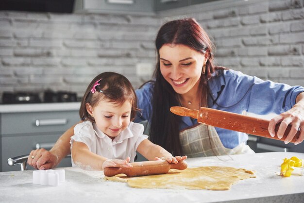 Glückliche Familie in der Küche. Holiday Food Konzept. Mutter und Tochter bereiten den Teig vor und backen Kekse. Glückliche Familie bei der Herstellung von Keksen zu Hause. Hausgemachtes Essen und kleiner Helfer