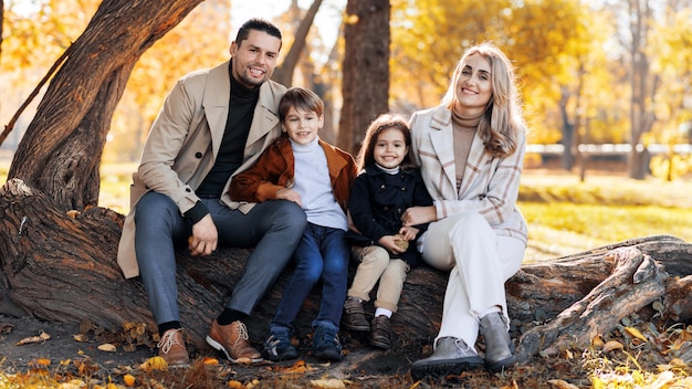 Glückliche Familie in einem Herbstpark Mutter, Vater, Sohn und Tochter sitzen auf einem Baumstamm