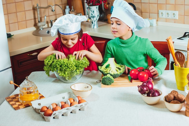 glückliche Familie lustige Kinder bereiten den frischen Gemüsesalat in der Küche vor