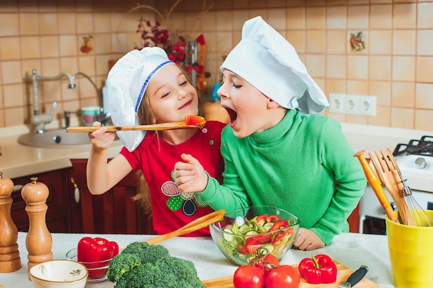 glückliche Familie lustige Kinder bereiten den frischen Gemüsesalat in der Küche vor