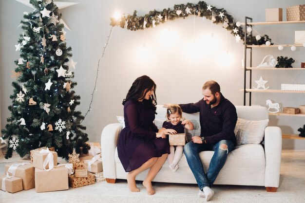 Glückliche Familie mit Kind sitzt auf dem Sofa neben dem Weihnachtsbaum und entspannt sich