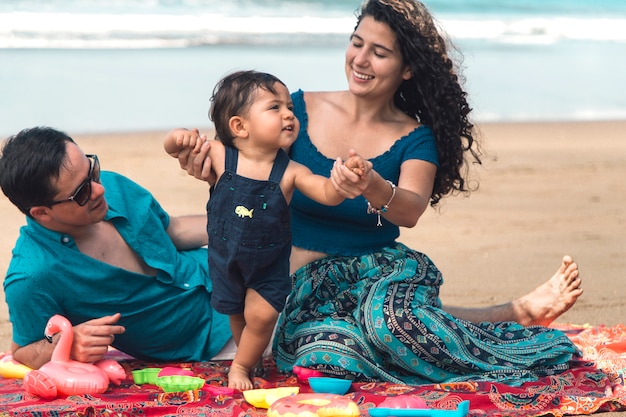 Glückliche Familie spielen und Baby lernen, am Strand zu gehen