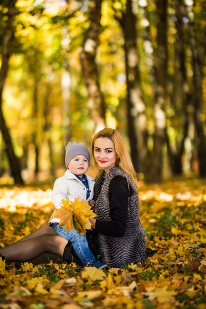 Glückliche Familienmutter, die mit Kind im Herbstpark nahe Baum spielt, der auf gelben Blättern liegt. Herbstkonzept.