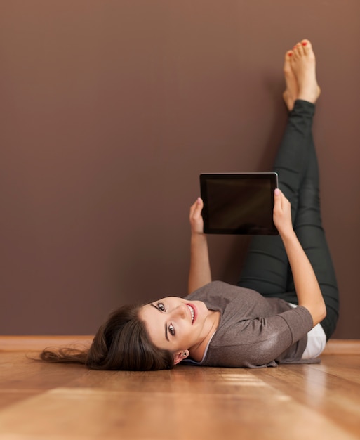 Glückliche Frau, die auf Boden mit digitalem Tablett liegt