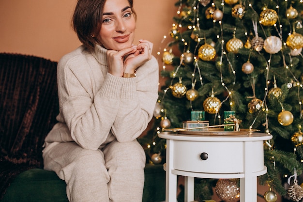 Glückliche Frau, die auf Sofa durch den Weihnachtsbaum sitzt