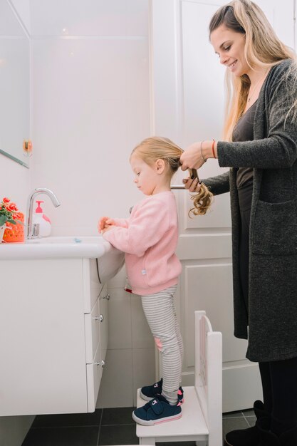 Glückliche Frau, die das Haar ihrer Tochter bindet